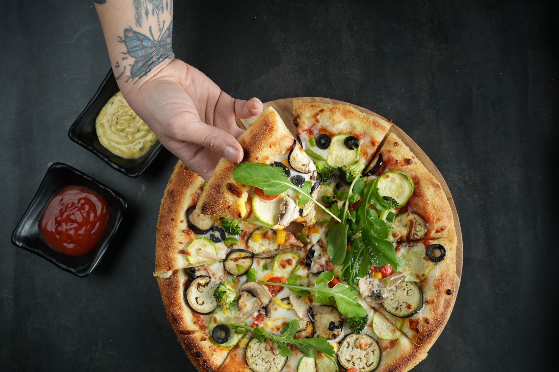 Dłoń sięga po kawałek pizzy wegetariańskiej